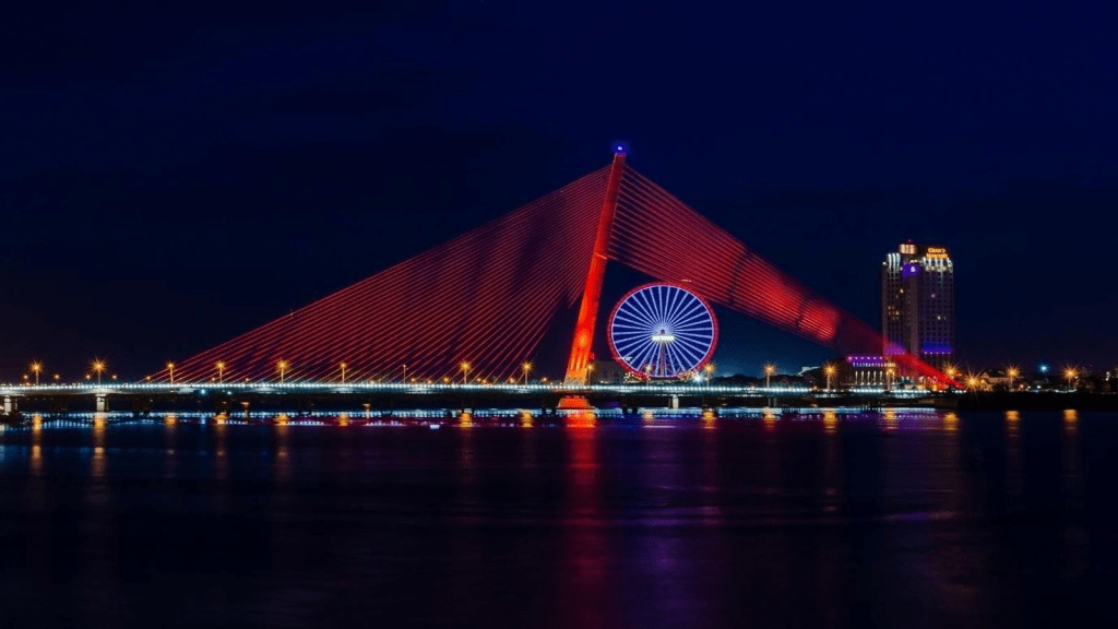 Tran Thi Ly Bridge at night, showcasing striking red and blue lights against a dark sky and shimmering water.
