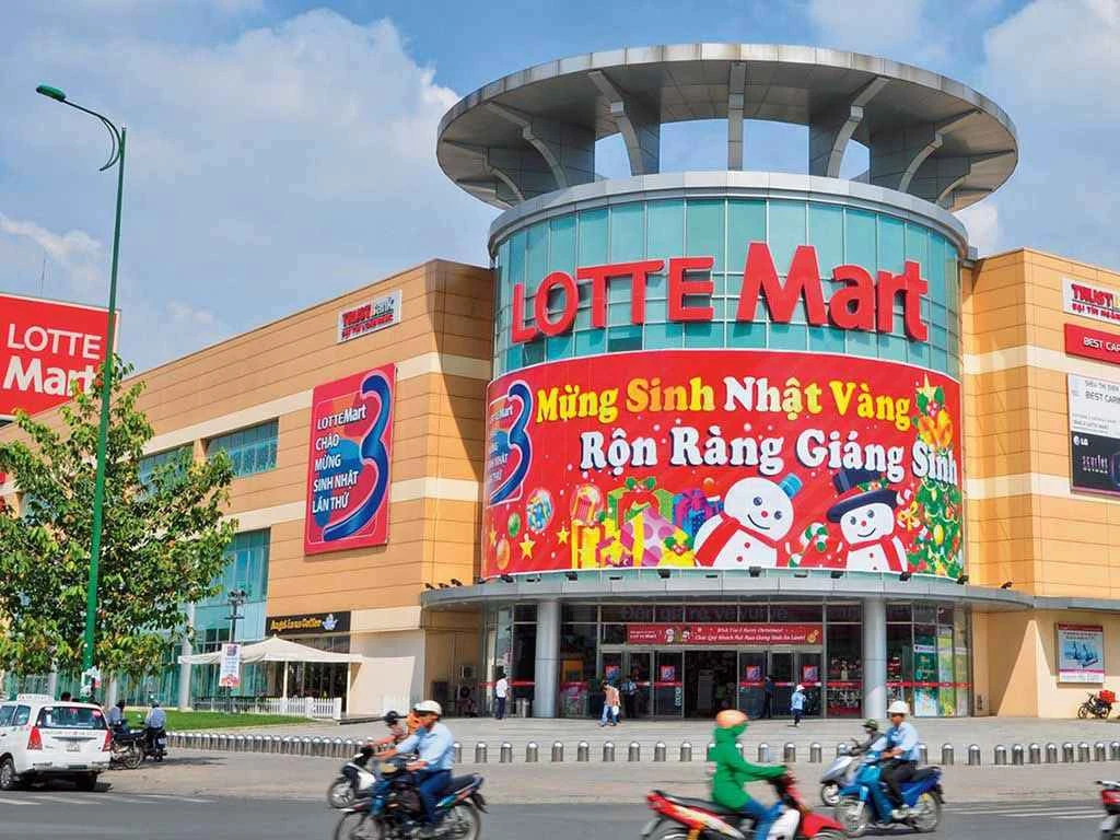 A bustling shopping center featuring motorcycles and pedestrians, with a supermarket visible in the background.