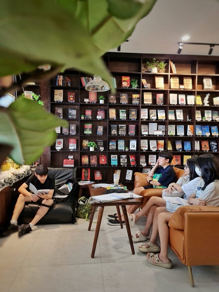 Many people are seated, engrossed in reading books at Hạnh Phúc Café, with a sleek black bookshelf in the background.