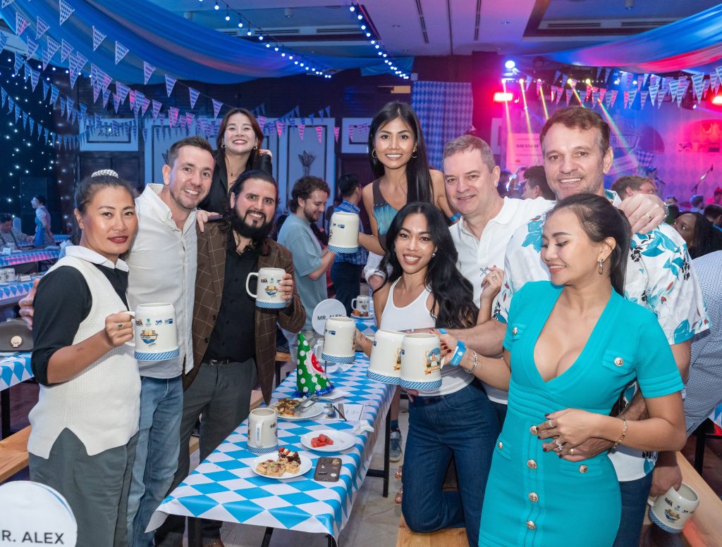 A group of people joyfully posing for a photo at an Oktoberfest celebration, surrounded by festive decorations and drinks.