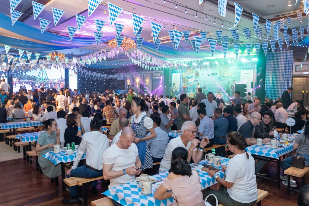 A lively restaurant scene during Oktoberfest, featuring patrons seated at tables adorned with blue and white bunting.