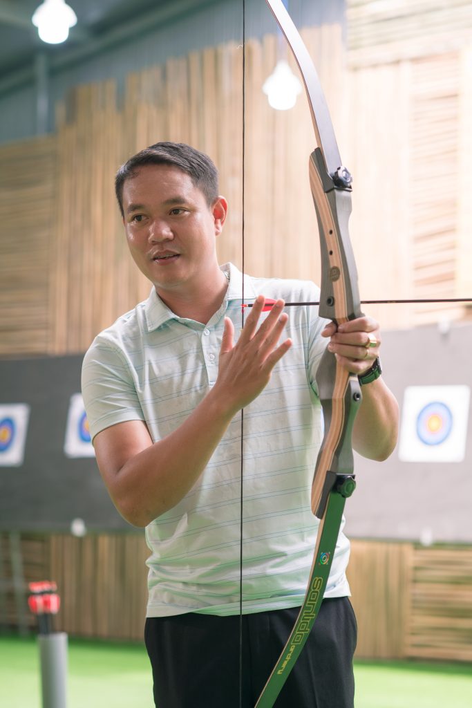 A man instructing others on how to shoot a bow, providing guidance during an archery lesson.