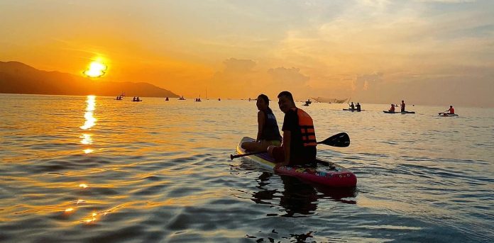 A person paddleboarding on calm waters under the sunrise at Man Thai beach.