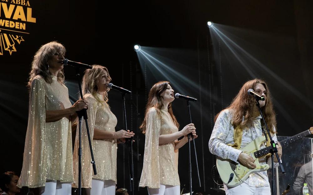 ABBA performs energetically on stage at a vibrant festival, captivating the audience with their iconic music.
