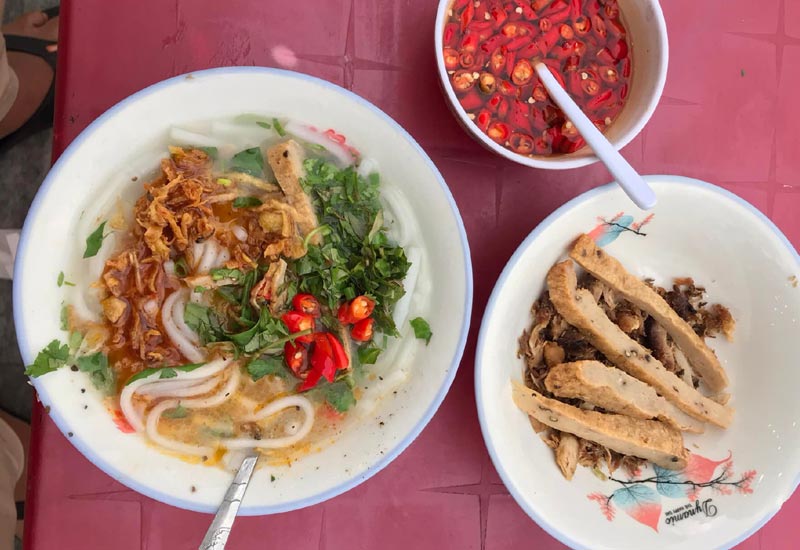 1 tô bánh canh cá cô Cúc cơ bản có rau thơm, ớt xắt, hành phi.Bên cạnh là 1 tô topping chả cá + cá khô , 1 chén nước mắm ớt xắt.