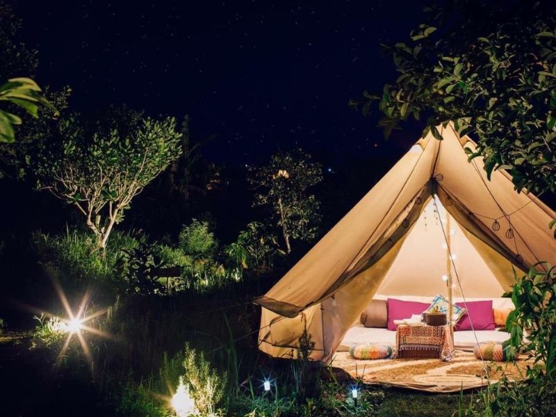 Overnight camping service at Suoi Mo Da Nang, with tents set up amidst lush natural scenery and warm campfire.