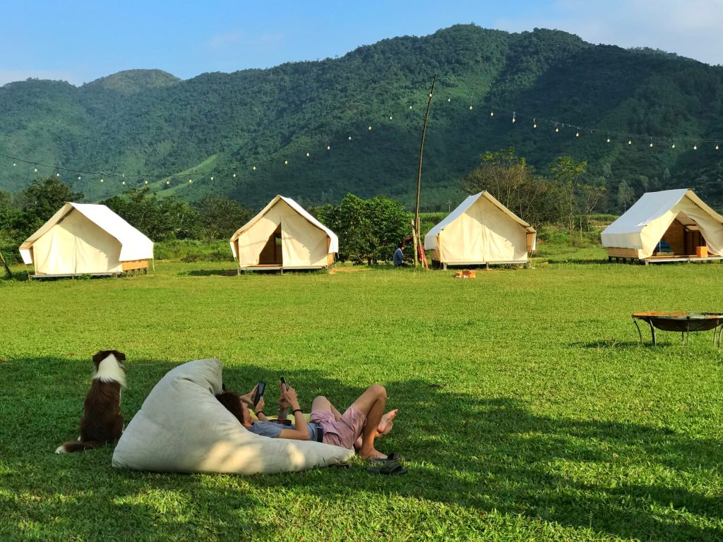 A serene landscape at Yen Retreat, showcasing lush greenery, calm waters of the Cu De River, and majestic mountains in the background, inviting visitors to unwind and reconnect with nature.