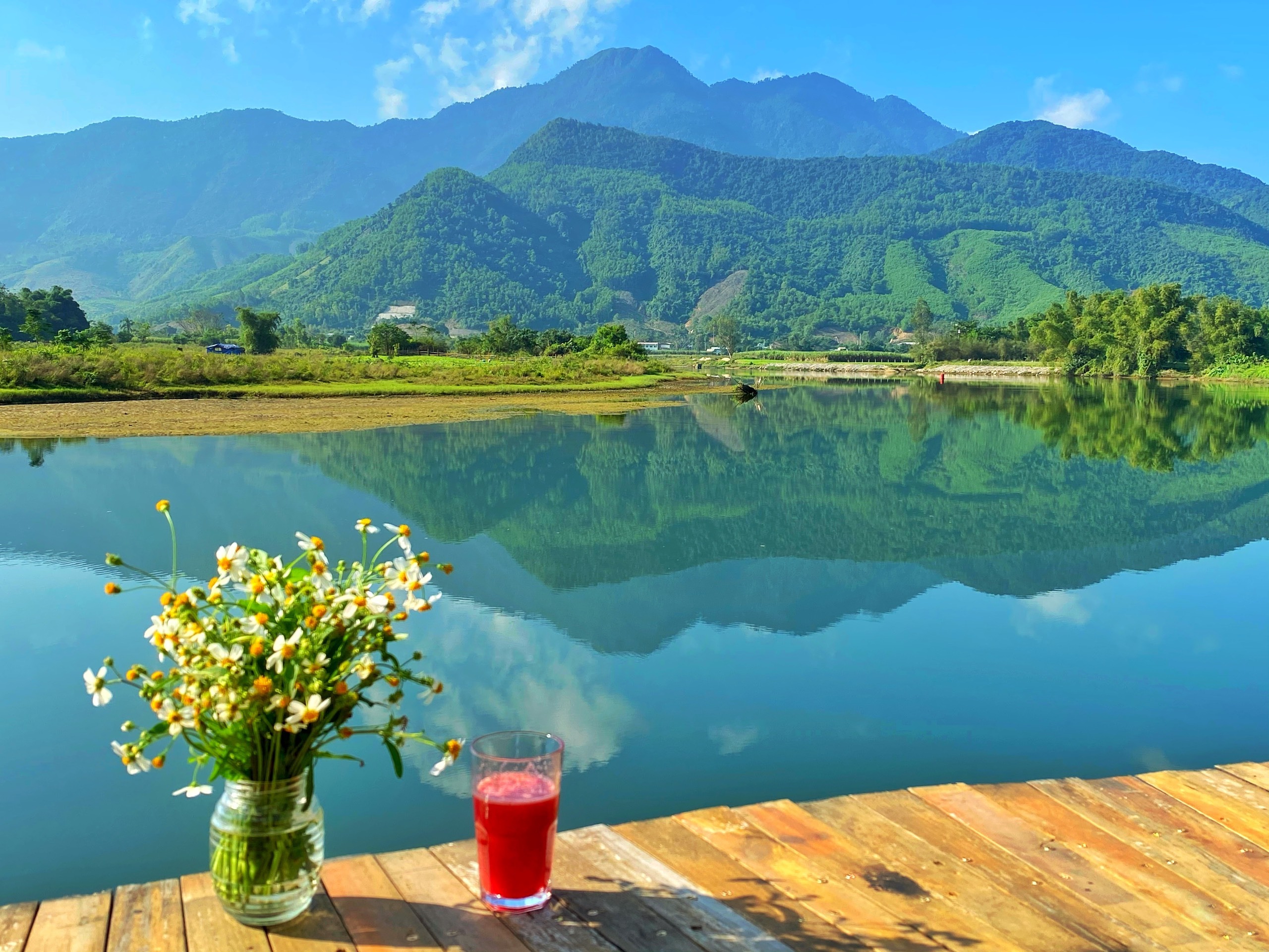 A serene view of the Cu De River winding through lush greenery with majestic mountains in the background.